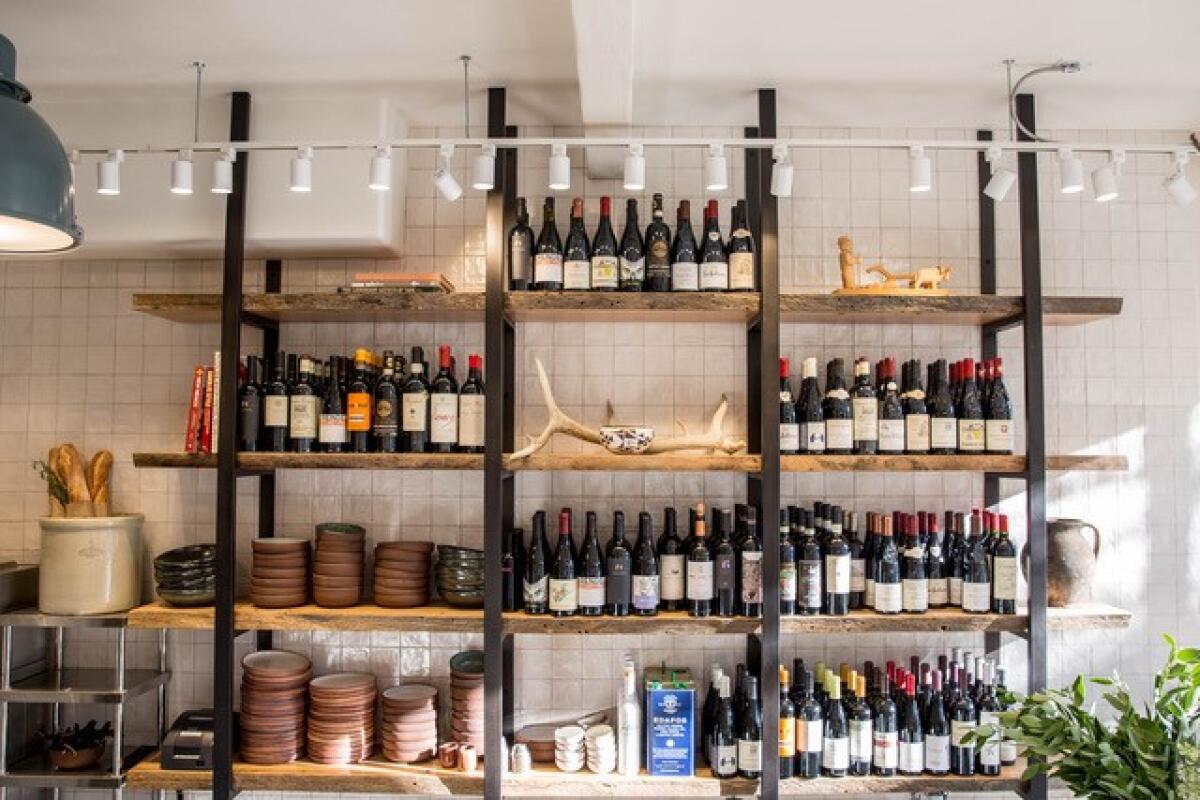 wood racks hold assorted wine bottles in front of a white tiled wall at a restaurant