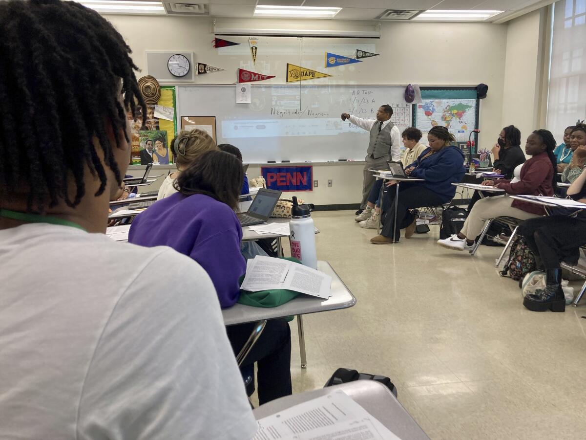 A teacher points at a white board as students look on