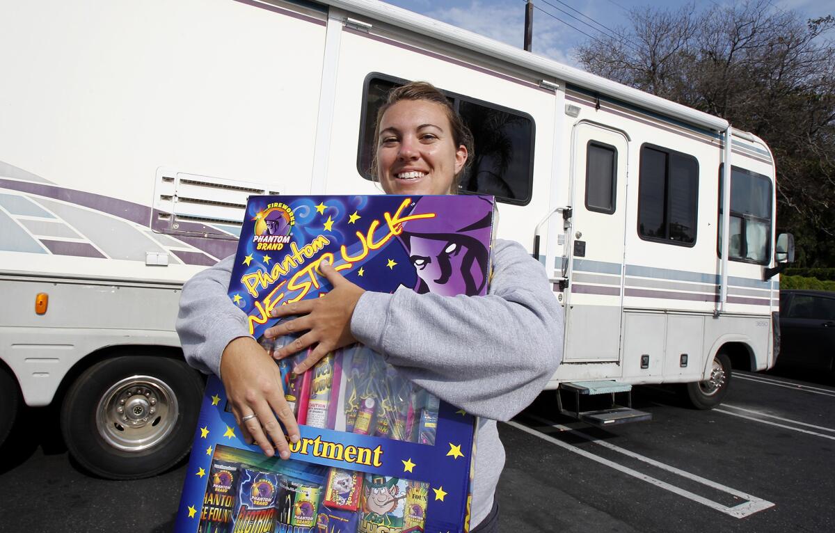 Youth group leader Christina Elliston holds one of the bigger packages of fireworks she has been watching over by spending the night on site since Saturday at the Victoria Street and Harbor Avenue Phantom Fireworks. She stays in a motor home borrowed from her grandparents. Sales raise money for kids from Canyon Community Church and Lighthouse Church to go to camp.