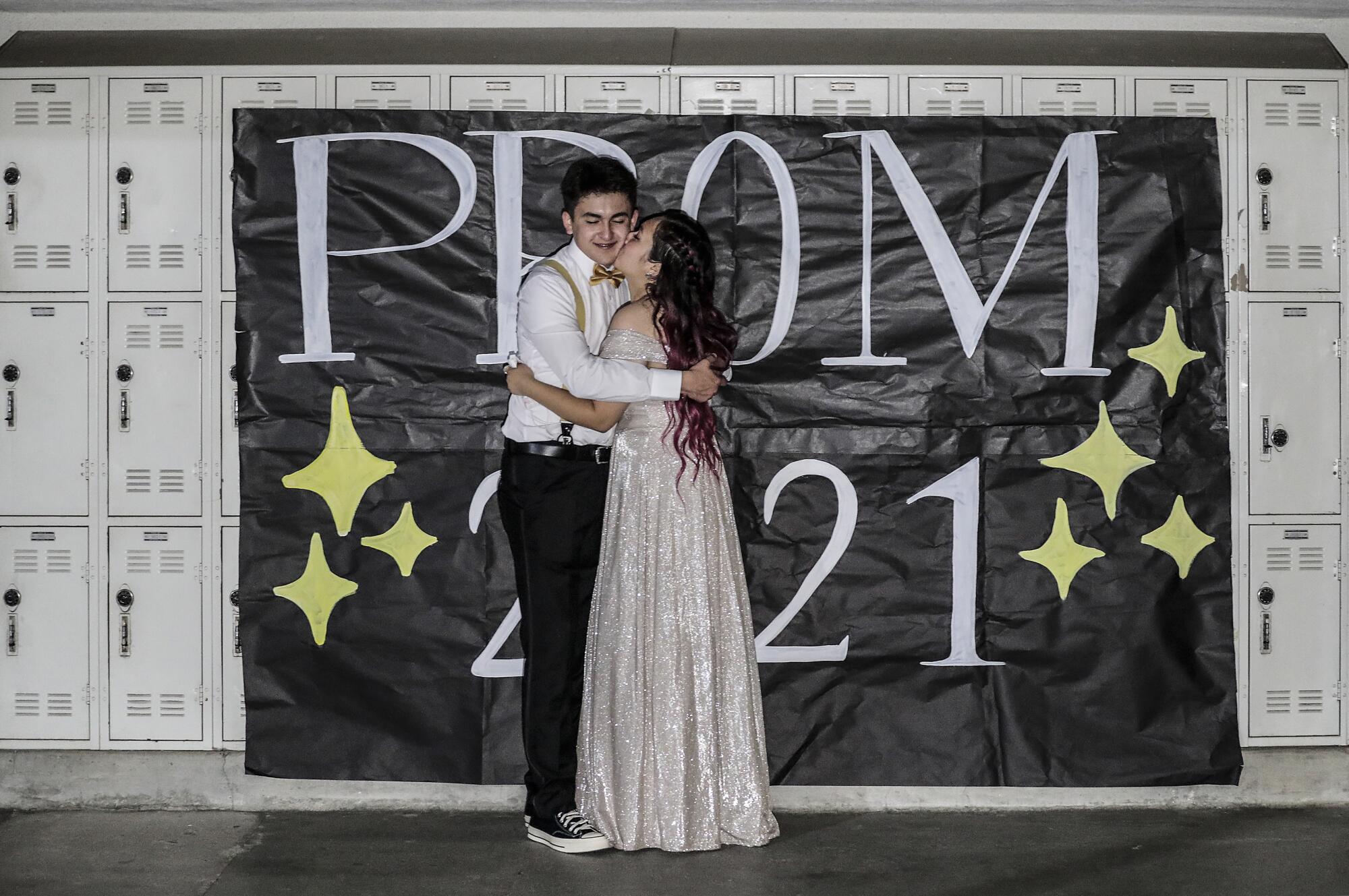 High school sweethearts embrace in front of lockers at their on-campus prom. 