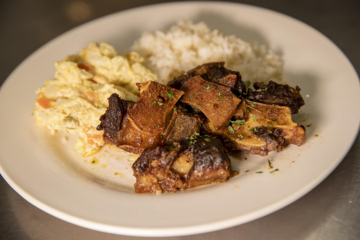 A plate of ox tails, white rice and potato salad 