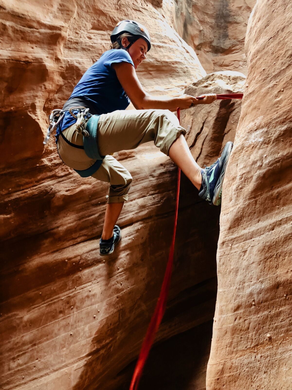 A woman climbs the wall of a slot canyon.