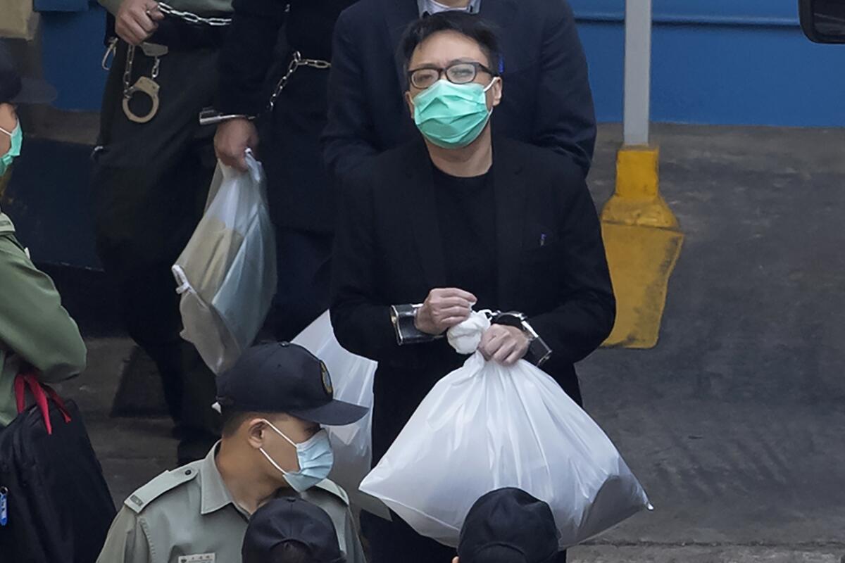 Tam Tak-chi, in handcuffs and holding a plastic bag, walks with officers
