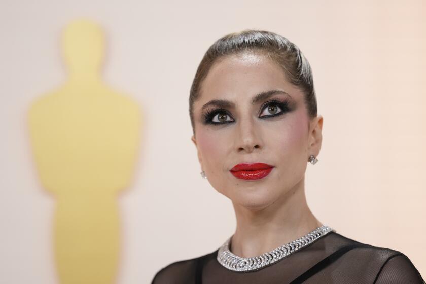 Lady Gaga poses in red lipstick, dark eye makeup and a sheer black dress with a silver collar.