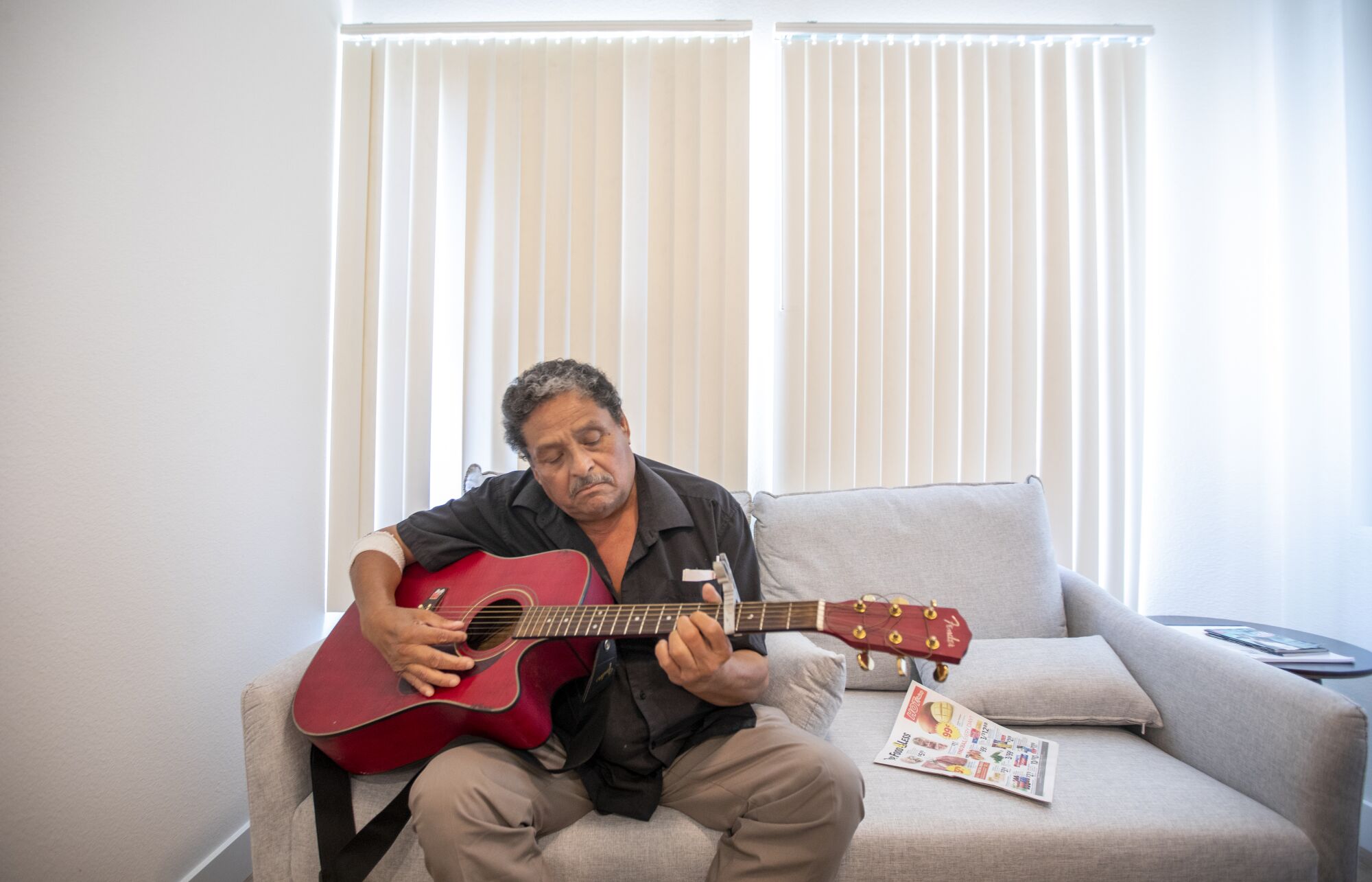 Angel Martinez plays his guitar inside his new home at Washington View Apartments in Los Angeles.