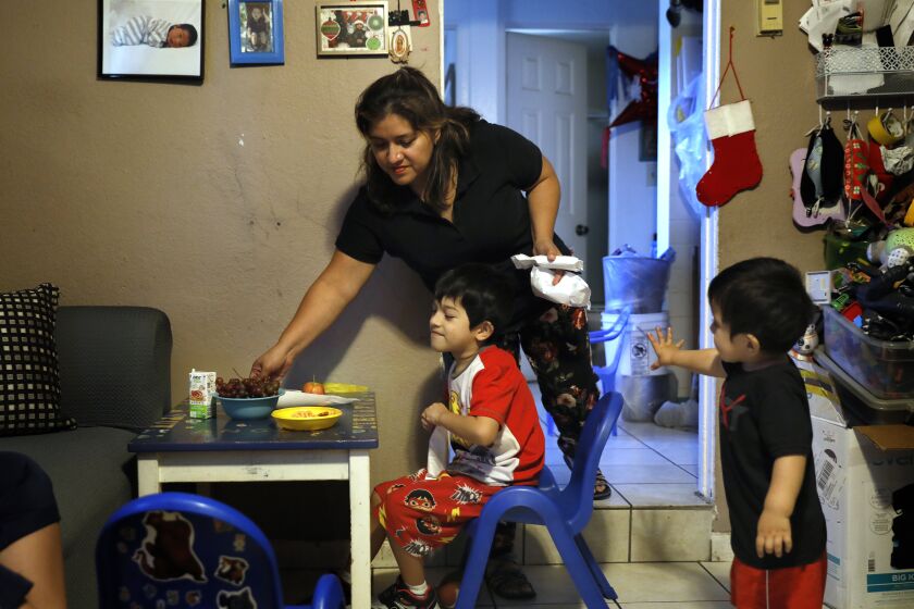 LOS ANGELES-CA-AUGUST 4, 2021: Glenda Valenzuela places snacks on the children's table as Daniel, 6, seated, and Alfredo, 2, right, look on at home in El Sereno on Wednesday, August 4, 2021. (Christina House / Los Angeles Times)
