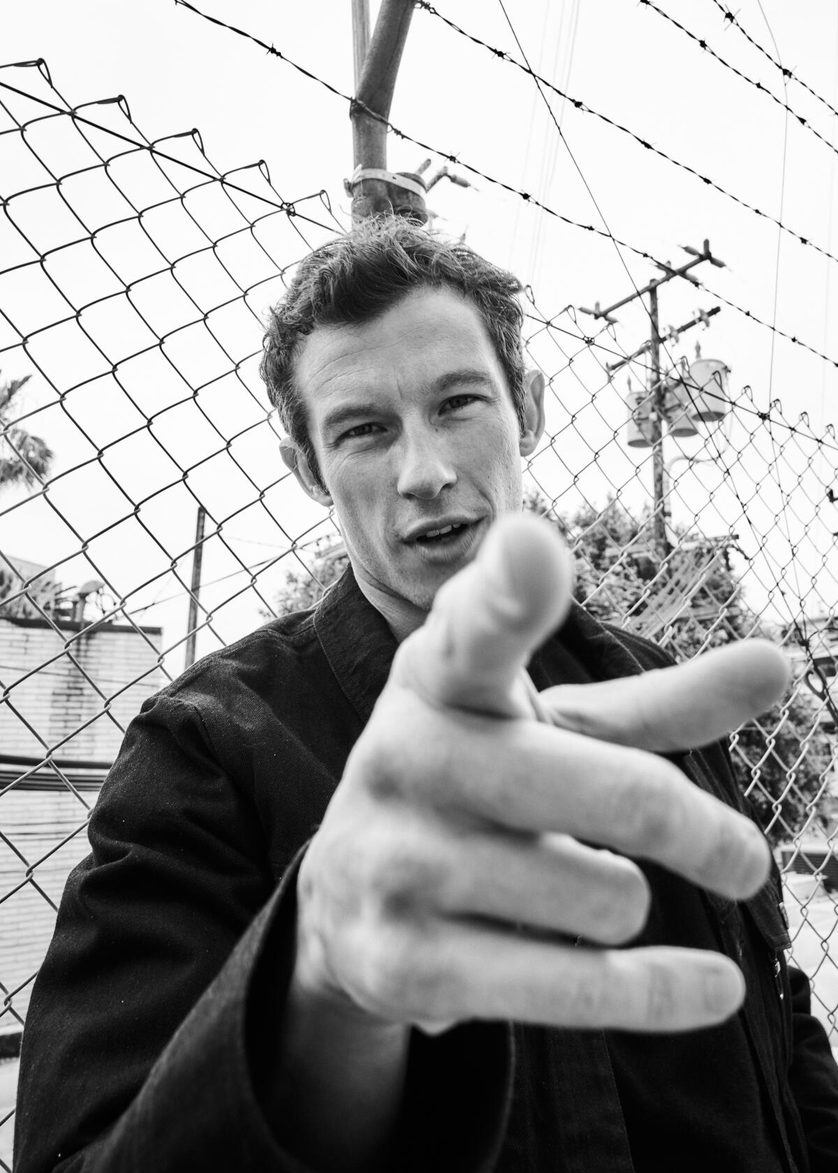 Callum Turner points his finger directly at the camera lens to take a portrait.