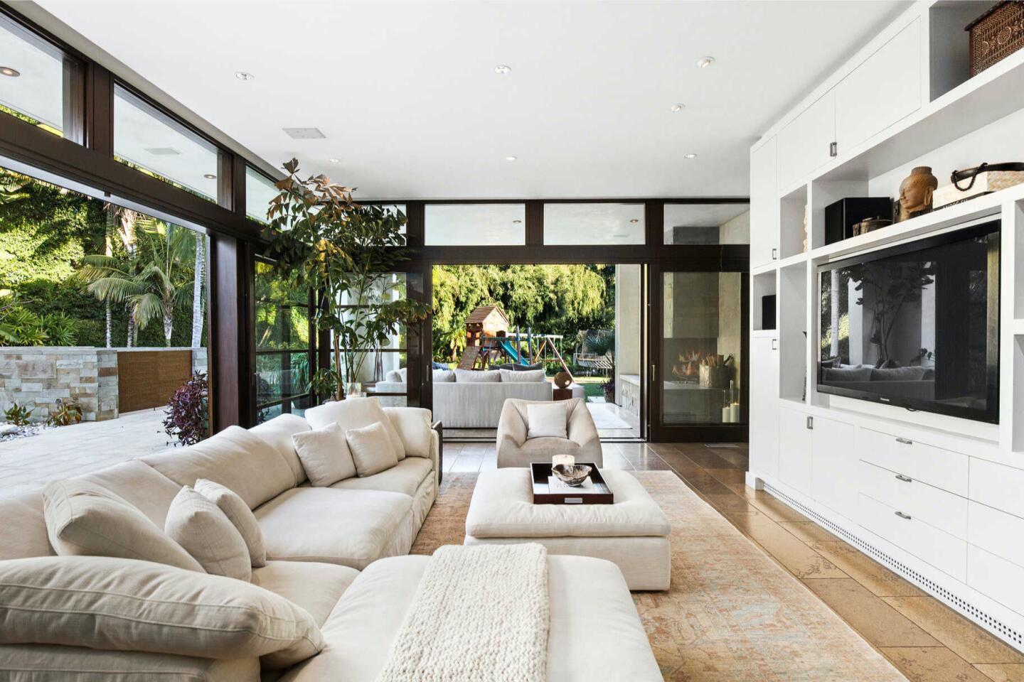 The furnished family room with a built-in TV and big windows looking out on trees.