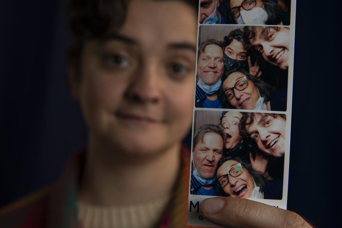A person holds up a photo-booth strip picturing them and three other people striking goofy poses