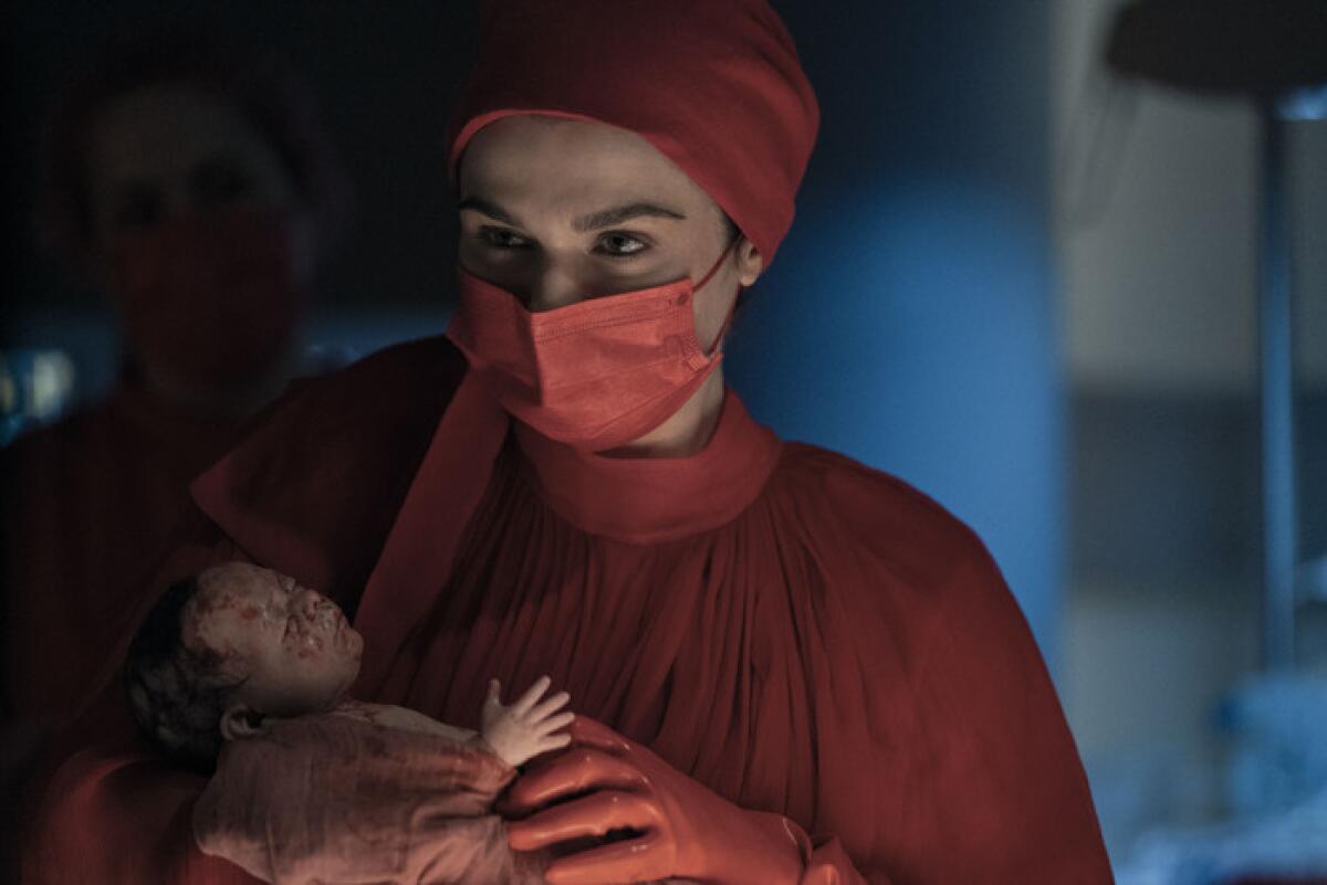 A doctor in red scrubs and a mask is holding a baby.