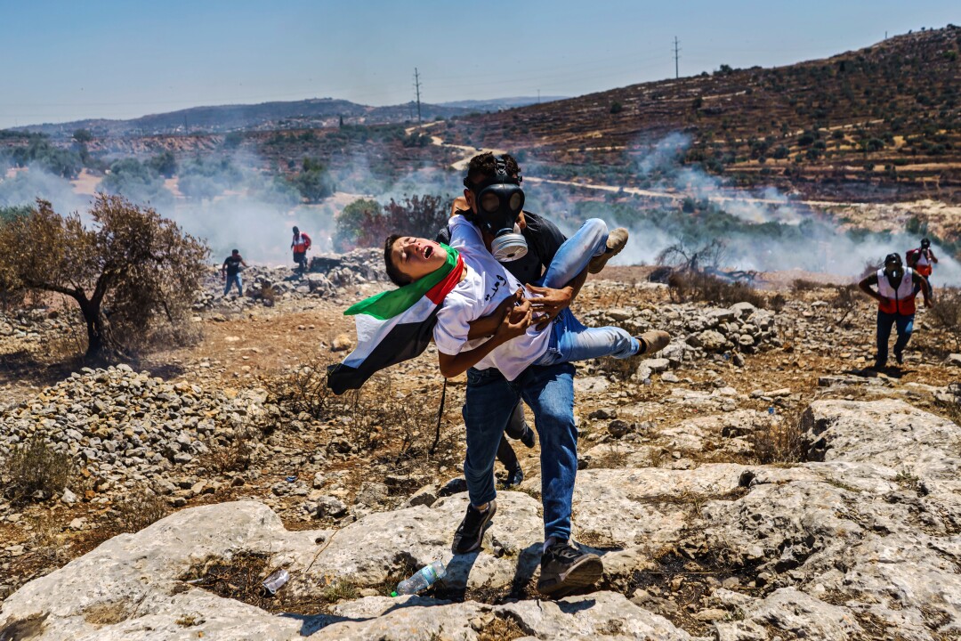 A Palestinian struggling to breathe is carried away from a protest amid smoke
