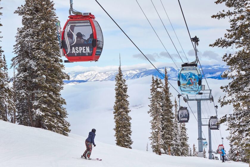 A woman skiing down a slope at Aspen Mountain with colorful gondolas overhead. Credit: Shawn O'Connor