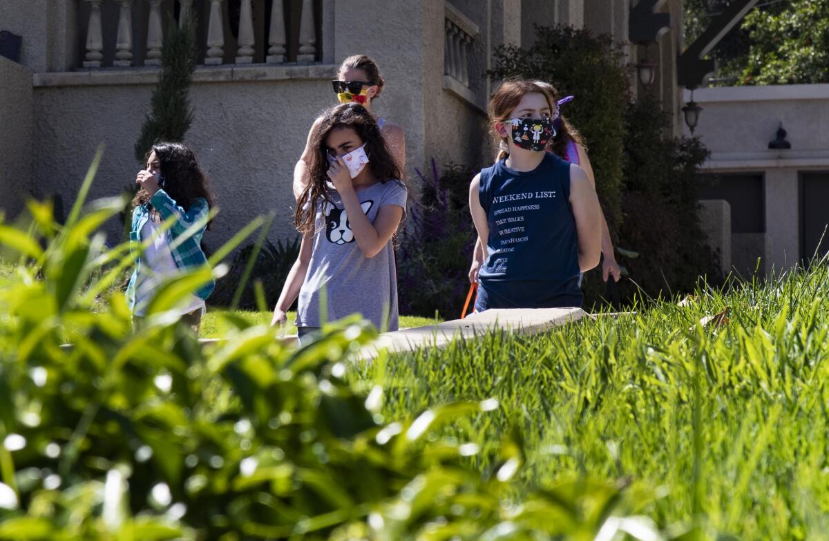  Wearing masks for protection, three school girls walk in their suburban neighborhood to a home cooking class.