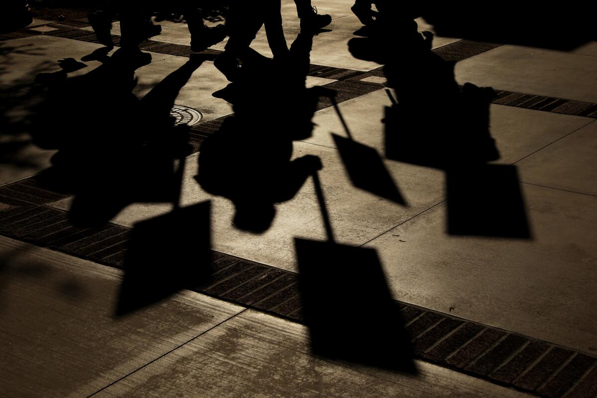 Silhouettes on the sidewalk of demonstrators picketing.