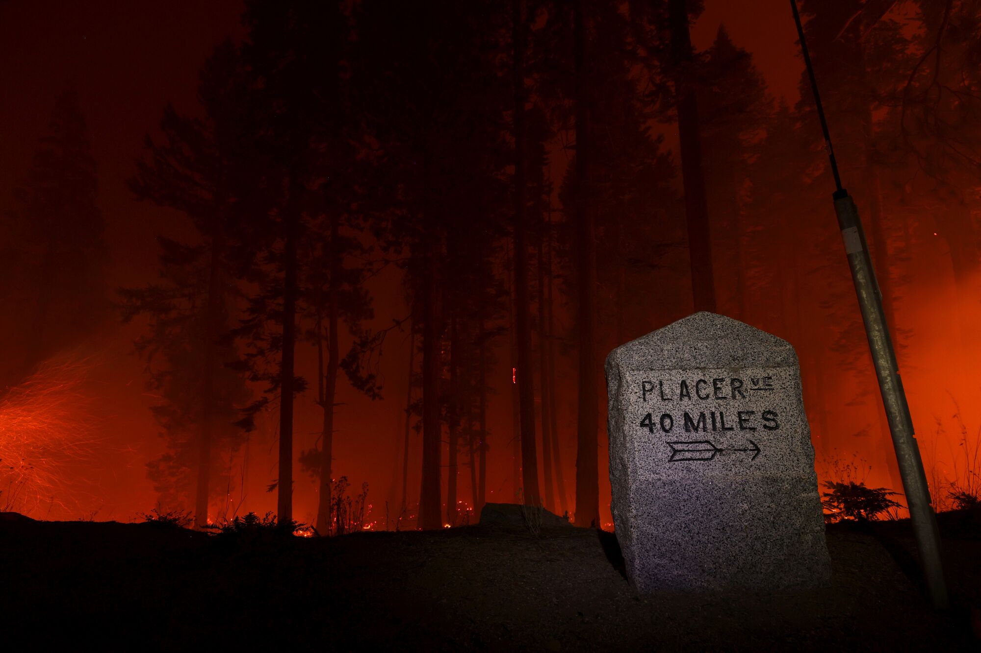 The Caldor fire glows behind a "Placerville: 40 Miles" mile marker along Highway 50.