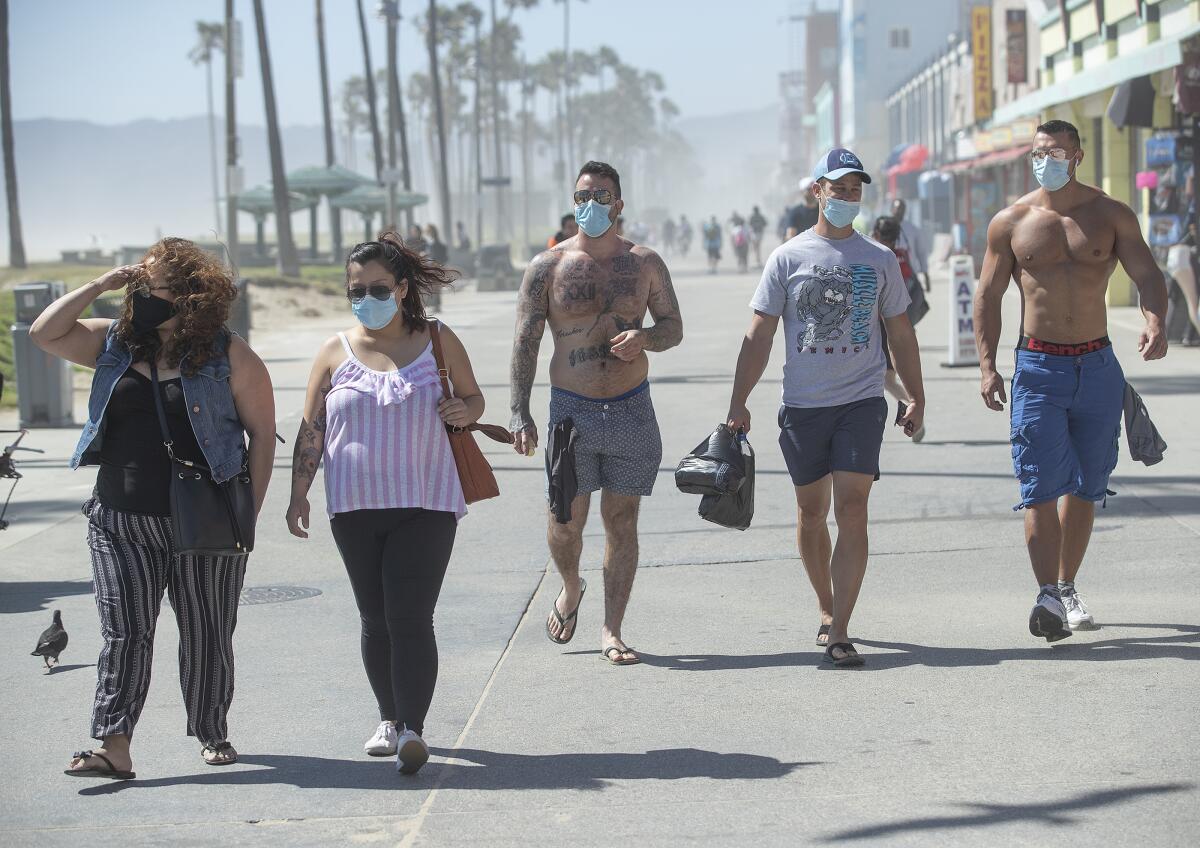 Visitors wearing masks walking along the boardwalk in Venice Beach.