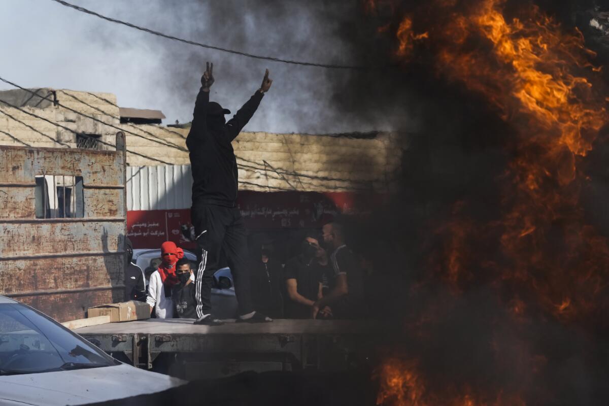 A man raises his arms during street protests as flames billow nearby.
