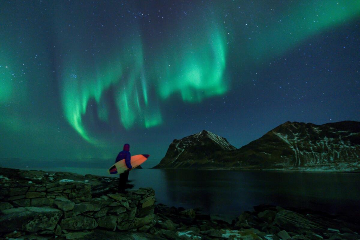 A surfer looks at the Northern Lights from the Lofoten islands in northern Norway.