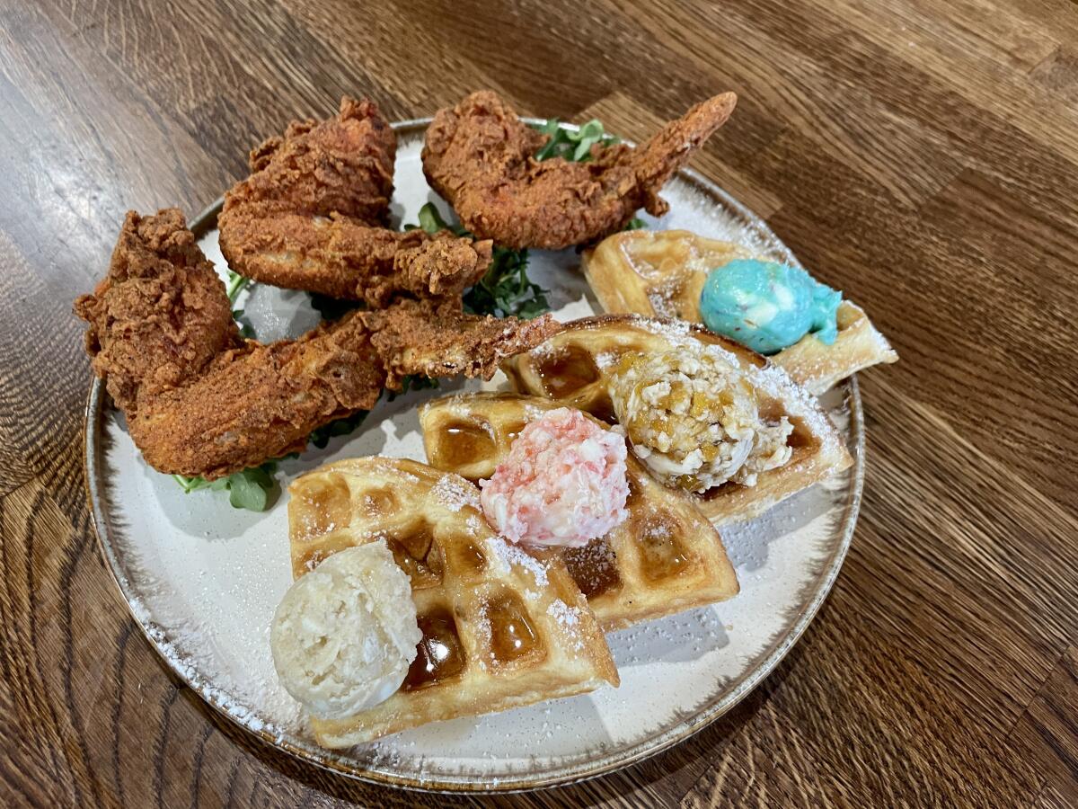 Fried chicken and a quartered waffle with different toppings on a white plate on a wooden table