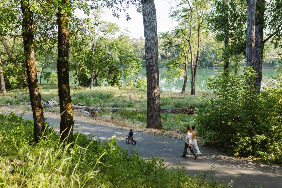 Two adults walk behind a child on a bike on the River Trail in Redding.