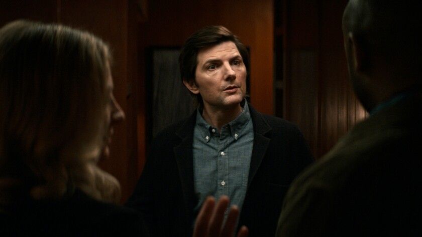 A man in a dark shirt in a dark room faces other people.