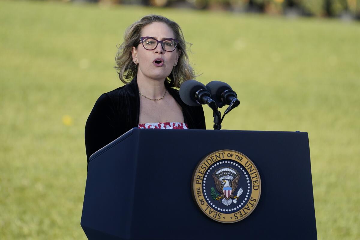 Sen. Kyrsten Sinema speaks from behind a lectern with the presidential seal outdoors