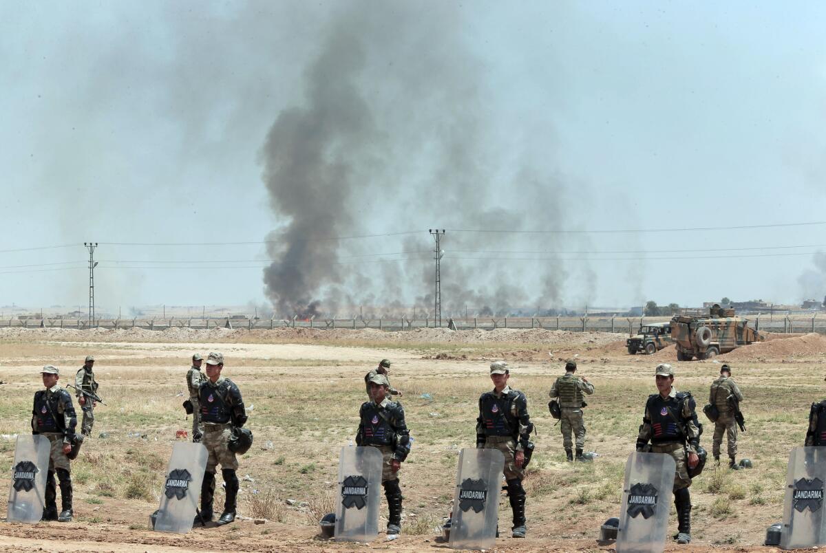 Turkish soldiers guard the border area with Syria in Akcakale, southeastern Turkey, as smoke from a fire caused by a U.S.-led airstrike rises over the outskirts of Tal Abyad, Syria.