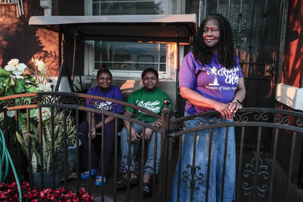 Lydia Friend stands at a gate with two children seated behind her.