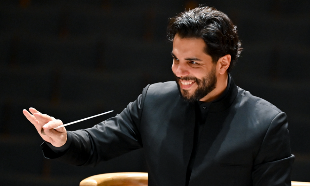 Domingo Hindoyan smiles and holds a conductor's baton in one hand.