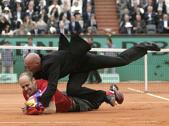 A security officer apprehends a trespasser on the court during the men's singles final match of the French Open between Roger Federer and Robin Soderling.