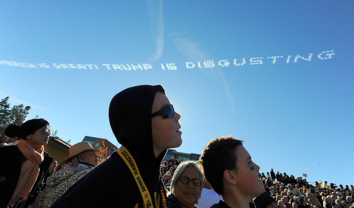 Parade spectators watch as an airplane writes the message, "America is great! Trump is disgusting," above the parade route during the 127th Rose Parade in Pasadena, Calif., on Jan. 1, 2016.