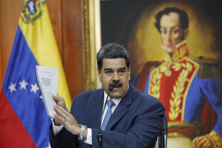 Venezuelan President Nicolas Maduro holds up a copy of his country's case taken to the International Criminal Court regarding U.S. sanctions during a press conference at Miraflores presidential palace in Caracas, Venezuela, Friday, Feb. 14, 2020. Venezuela is demanding that Washington stop piling on punishing financial sanctions aimed at forcing a regime change in Venezuela. The international court must next decide whether it will open an investigation. (AP Photo/Ariana Cubillos)