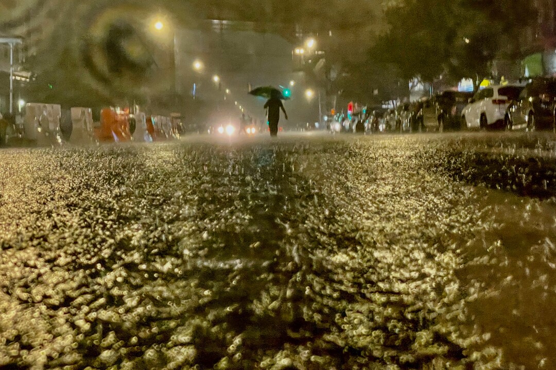 مردی با چتر در خیابان زیر باران شدید قدم می زند.