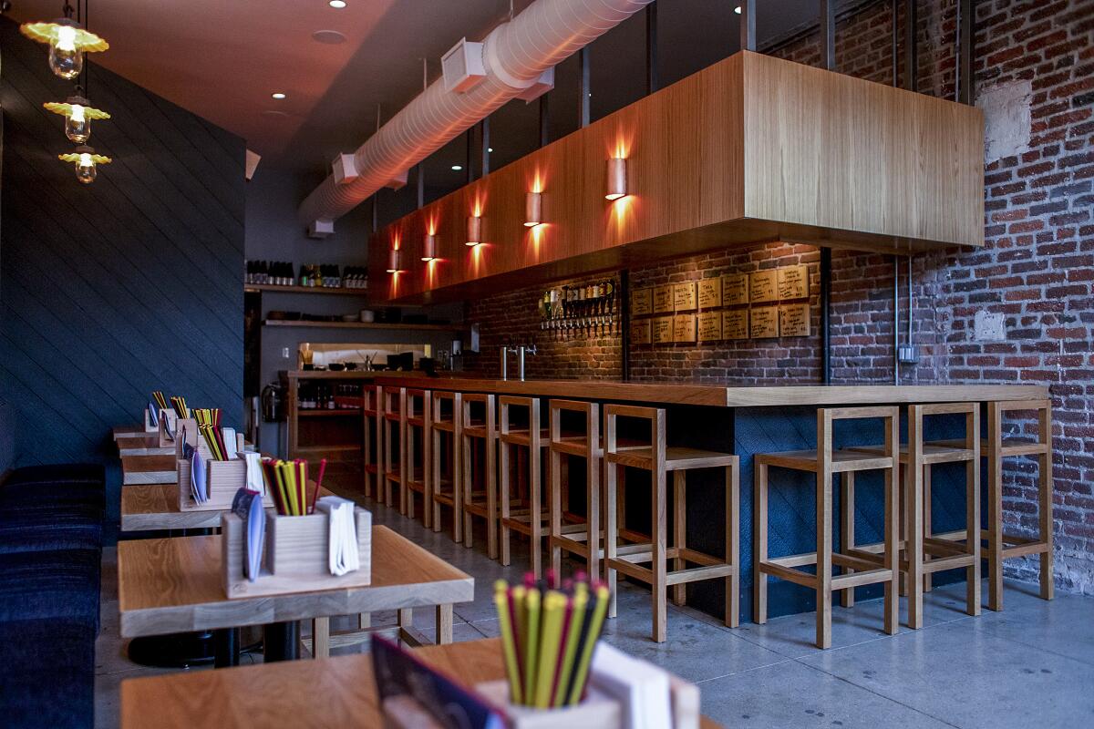 Inside of a restaurant with brick walls and a wooden bar with tall wood barstools