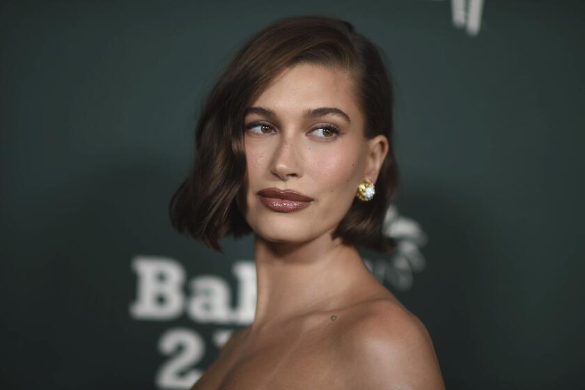 Hailey Bieber wearing short hair and silver earrings in a strapless dress against a dark backdrop
