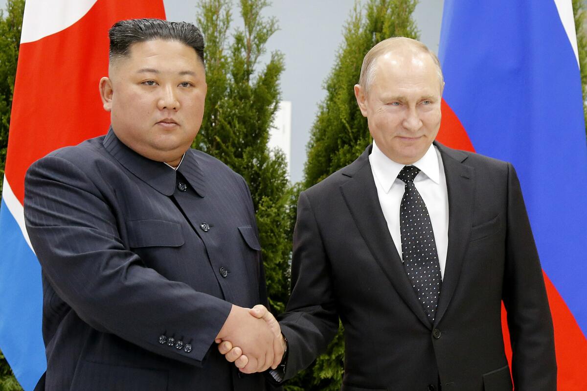 Kim Jong Un shaking hands with Vladimir Putin while standing before flags
