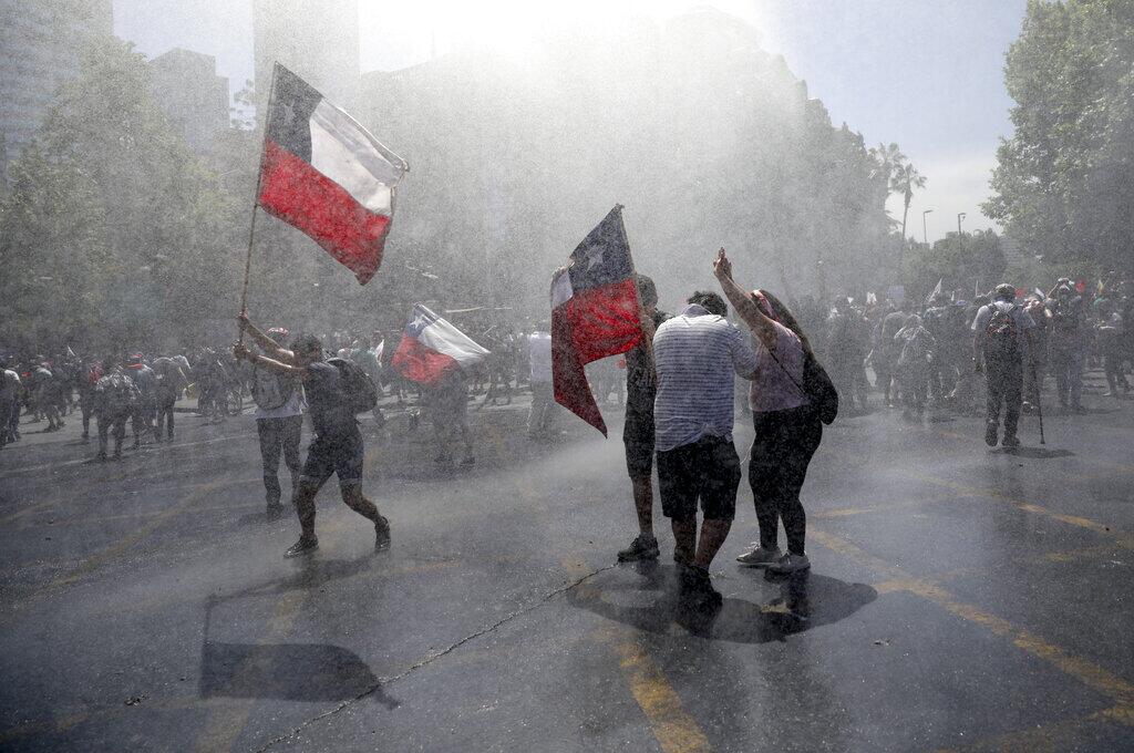 Manifestantes con banderas de Chile reciben chorros de agua lanzados por la policía en el centro de Santiago en una nueva jornada de protestas sociales en la nación sudamericana, el miércoles 23 de octubre de 2019. Chile enfrenta un estallido social alimentado por un alza en las tarifas del metro. (AP Foto/Rodrigo Abd)