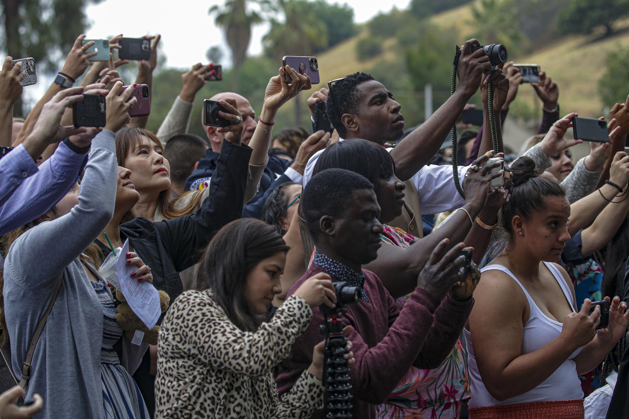 Family members of newly graduated police officers train their phones and cameras to take photos at the ceremony.