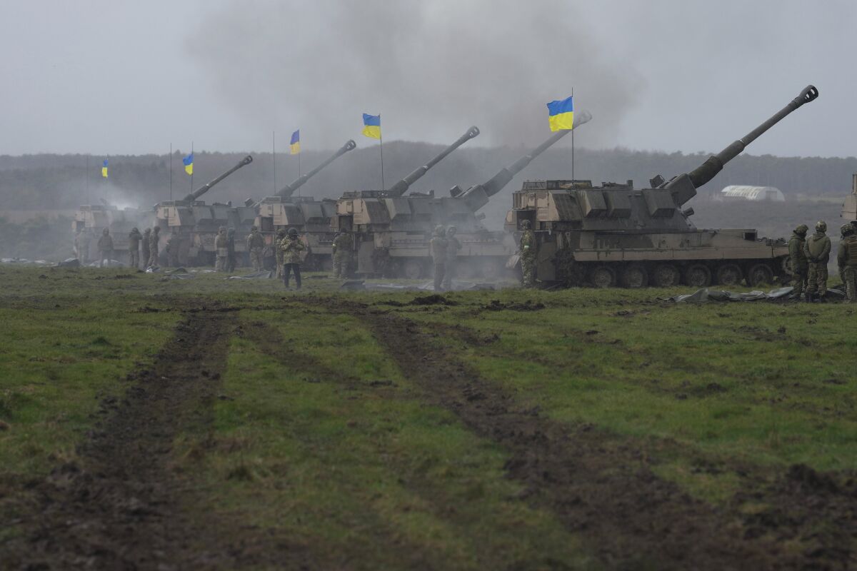 Tanks flying Ukrainian flags on a grassy field.
