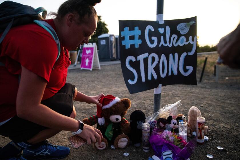 Kent Nishimura??Los Angeles Times LAURA MILLER places a stuffed bear at a makeshift memorial to the victims of the Gilroy Garlic Festival shooting. The gunman legally bought the AK-47-style rifle used in the July 28 attack weeks earlier in Nevada.