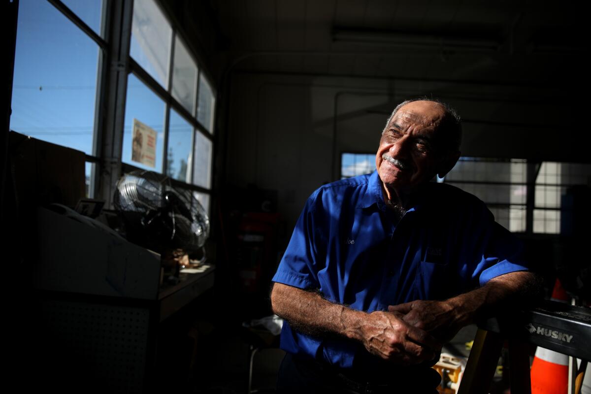 A man in a gas station uniform is illuminated by bars of light through a window. He smiles slightly.