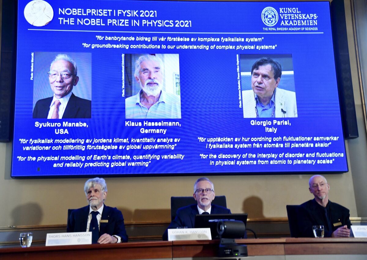Nobel Committee announcing physics prize with a big screen above them showing winners' photos