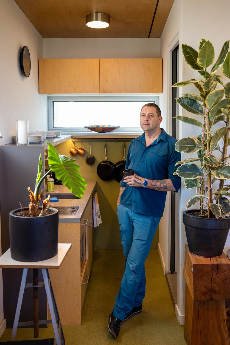 A man stands among potted plants in a galley kitchen.