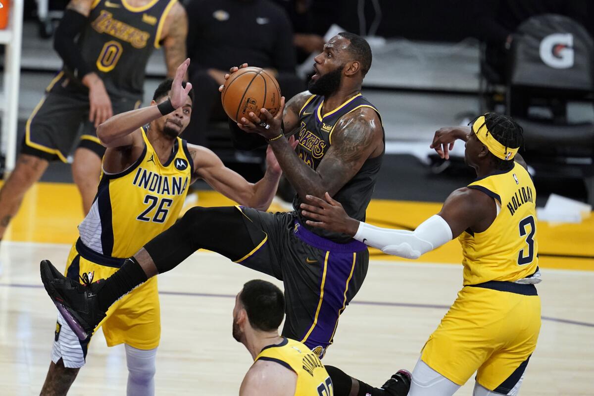The Lakers' LeBron James drives to the basket between the Pacers' Jeremy Lamb, left, and Aaron Holiday on March 12, 2021.