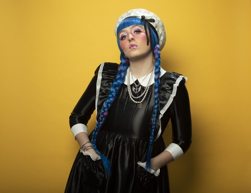 Ashnikko in a black dress, blue braids and a white hat.