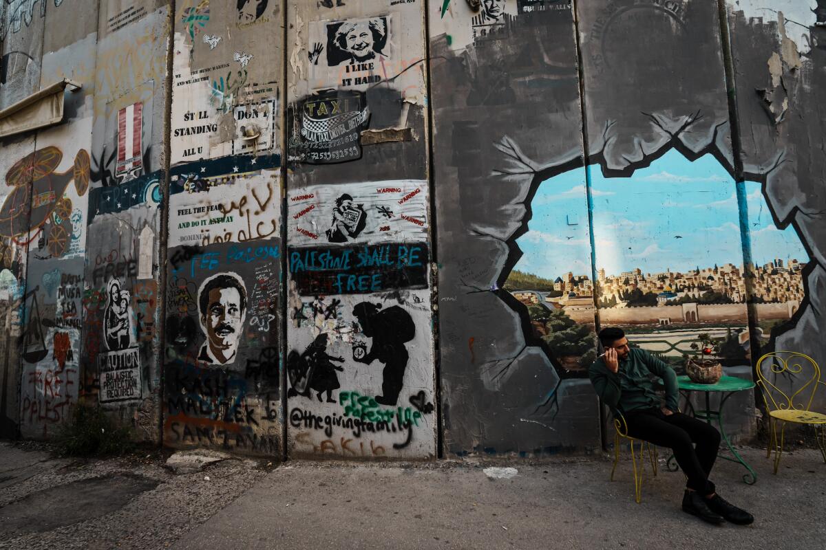 A man sits by a mural on a wall separating Bethlehem from Jerusalem.