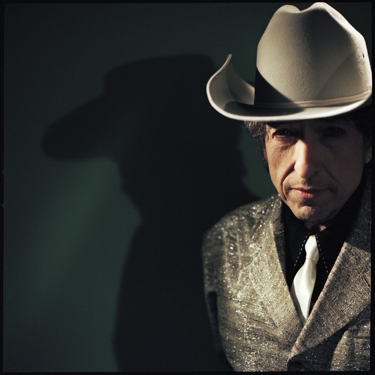 A man in a jacket, tie and cowboy hat.