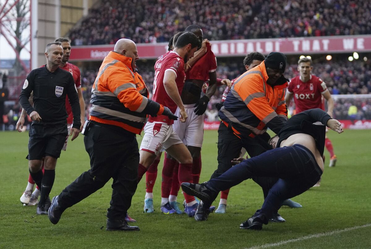 Stewards block a man who invaded the pitch as Nottingham Forest celebrate scoring their side's third goal, during the English FA Cup fourth round soccer match between Nottingham Forest and Leicester City at the City Ground, Nottingham, England, Sunday, Feb. 6, 2022. Police have arrested a man who appeared to attack Nottingham Forest players as they celebrated one of their goals in an FA Cup victory over Leicester. A supporter emerged from the away section of the City Ground before striking out at Forest players as they celebrated the third in a 4-1 win over the cup holders. (Tim Goode/PA via AP)