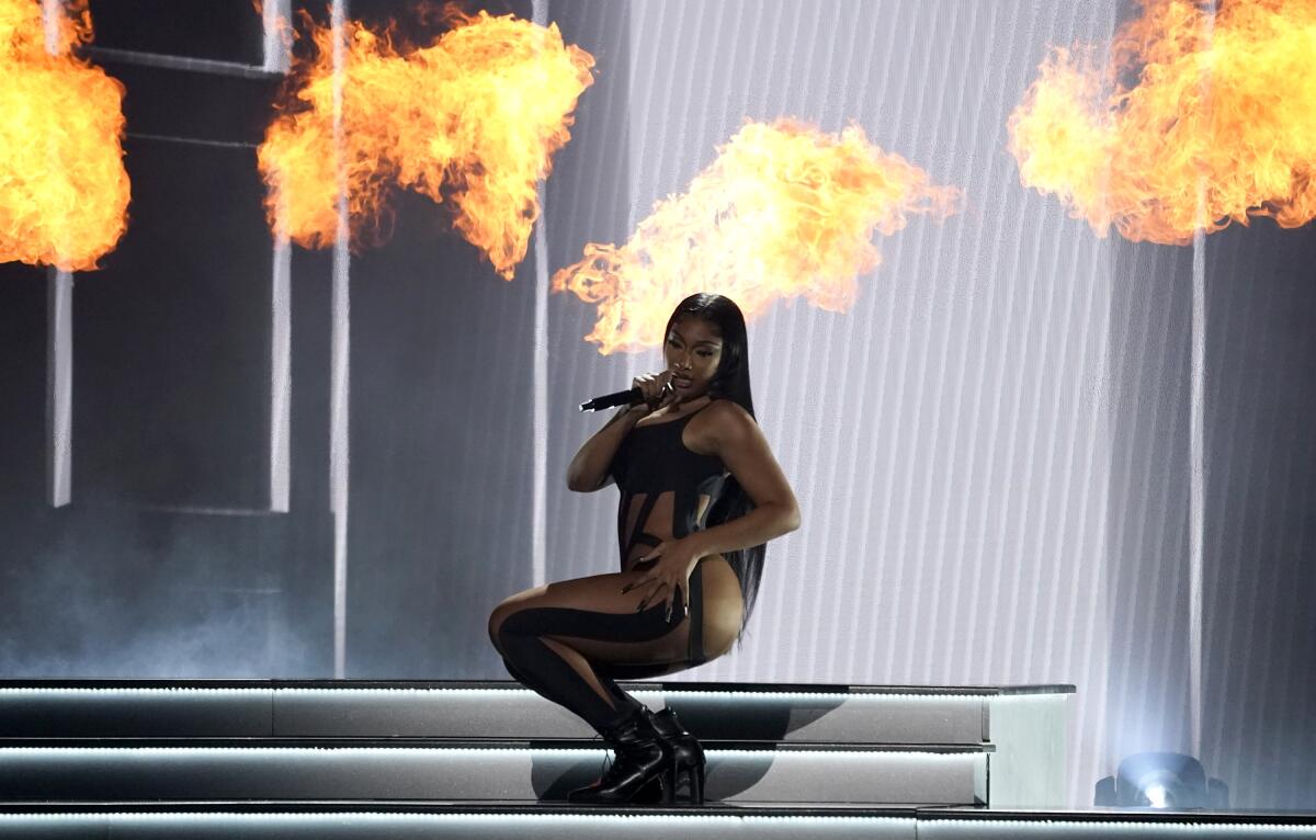 Megan Thee Stallion performs in a black catsuit and heels with balls of flame behind her. 