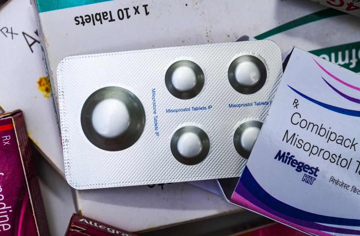 A blister pack of five pills partly inside a box reading "Combipack" and "Misoprostol," on top of other boxes of medication